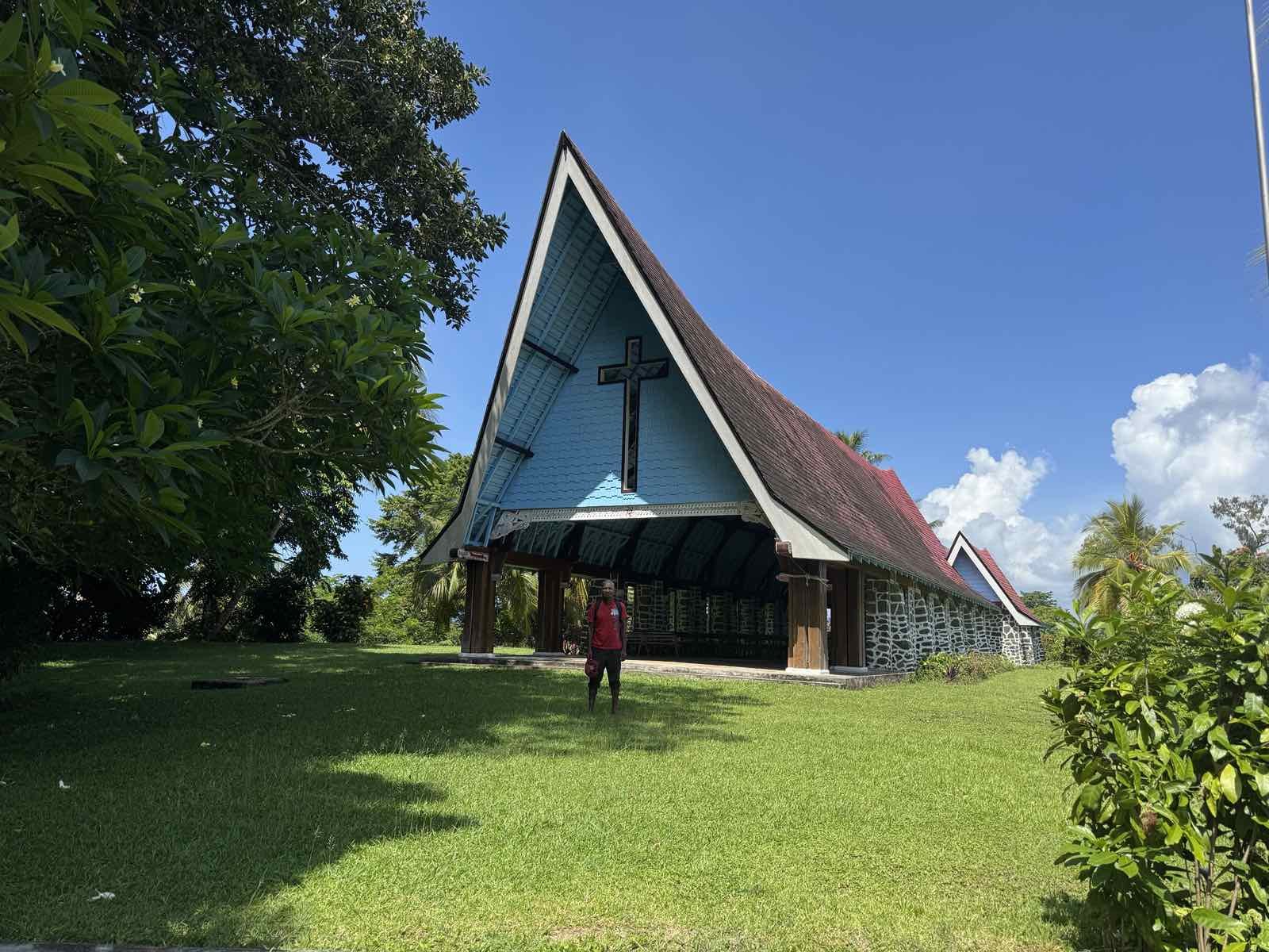 Kwato church building in Milne Bay Province with a cross on the front and tropical greenery around it